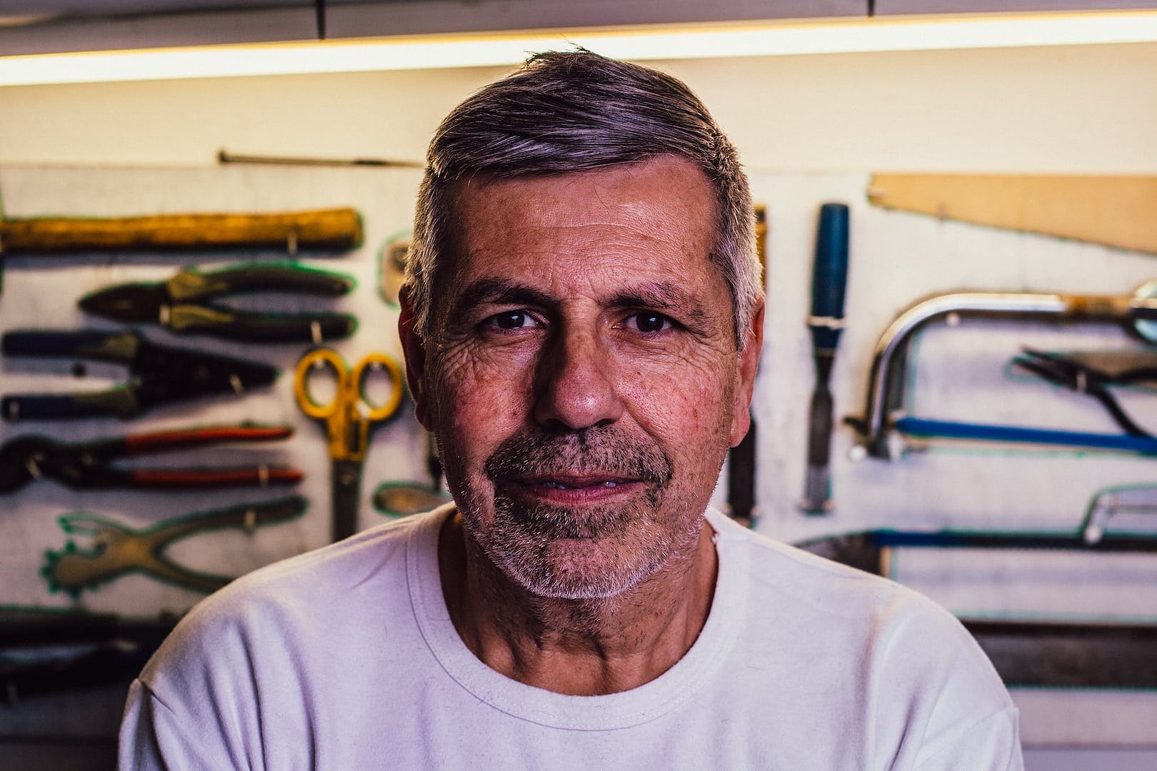 portrait photo of man in white crew neck t shirt with assorted hand tools in background
